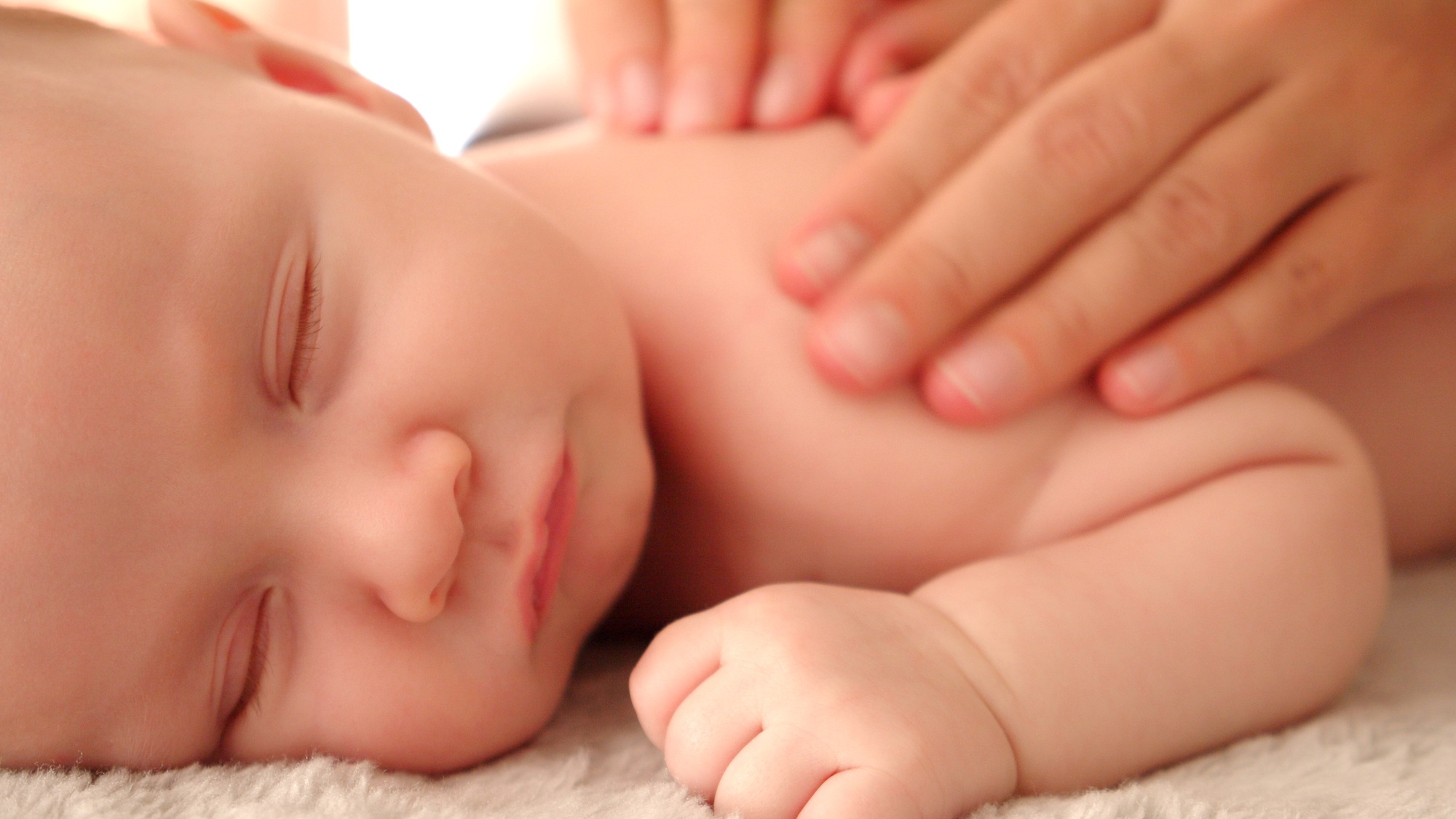 Mother doing massage on her healthy sleeping infant baby.